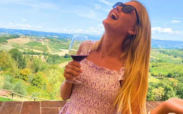 Woman enjoying wine with a view of Chianti vineyards on a guided tour in San Gimignano.