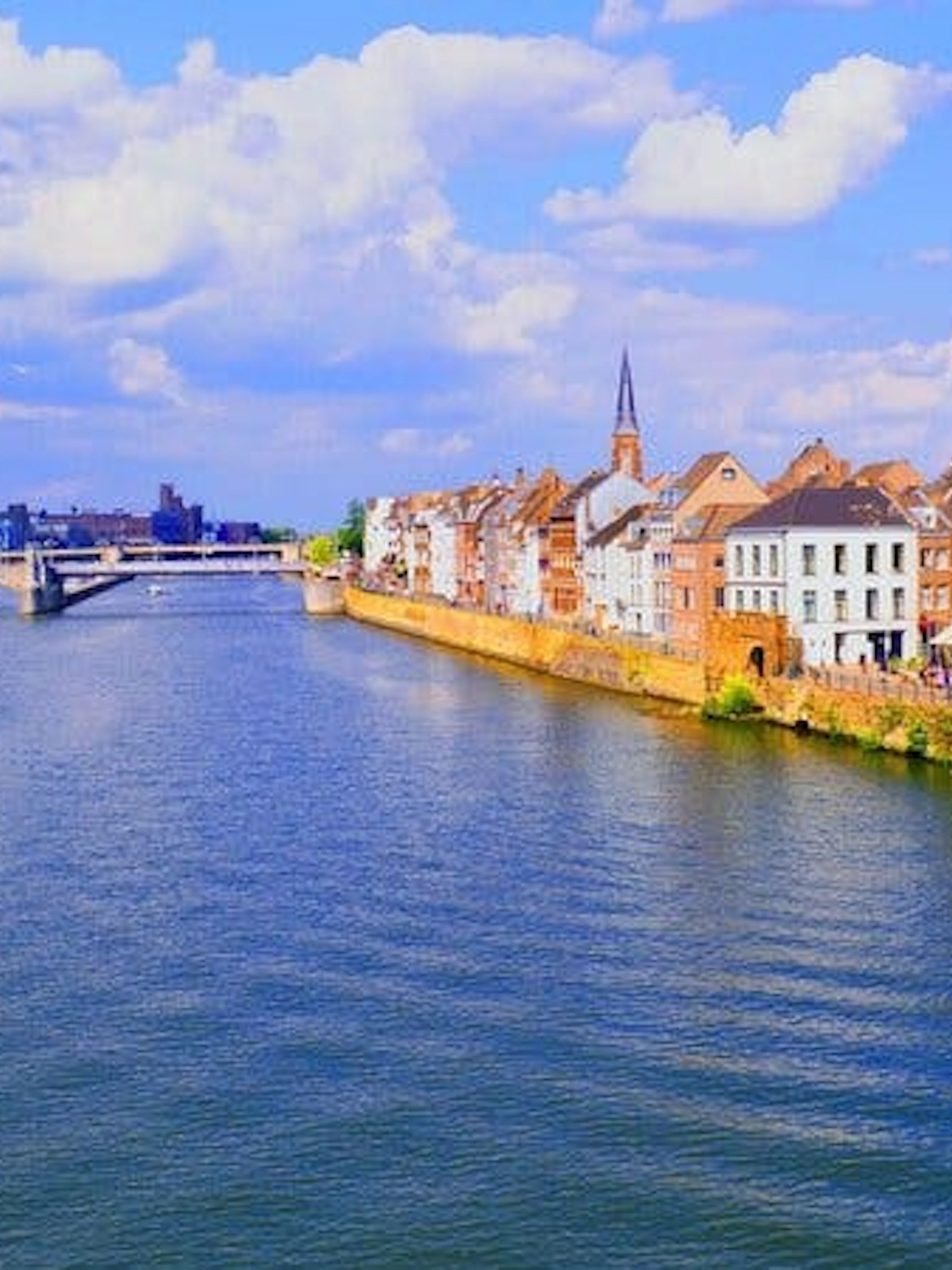 Maastricht riverfront with historic buildings and bridge on self-guided walking tour.