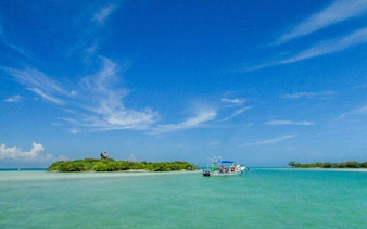 Boat approaching Pasion Island with clear turquoise water and blue sky, Holbox Island day trip.