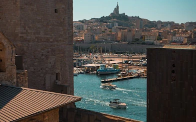Marseille harbor view with boats and Notre-Dame de la Garde basilica in the background.