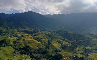 Sapa Muong Hoa Valley terraced rice fields with distant mountains under cloudy sky.