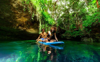 Snorkeling tour participants paddleboard in a lush cenote, surrounded by vibrant greenery.