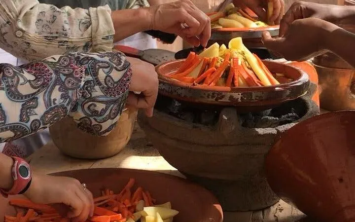 Hands preparing vegetables in a tagine during a Moroccan cooking class in Marrakesh.