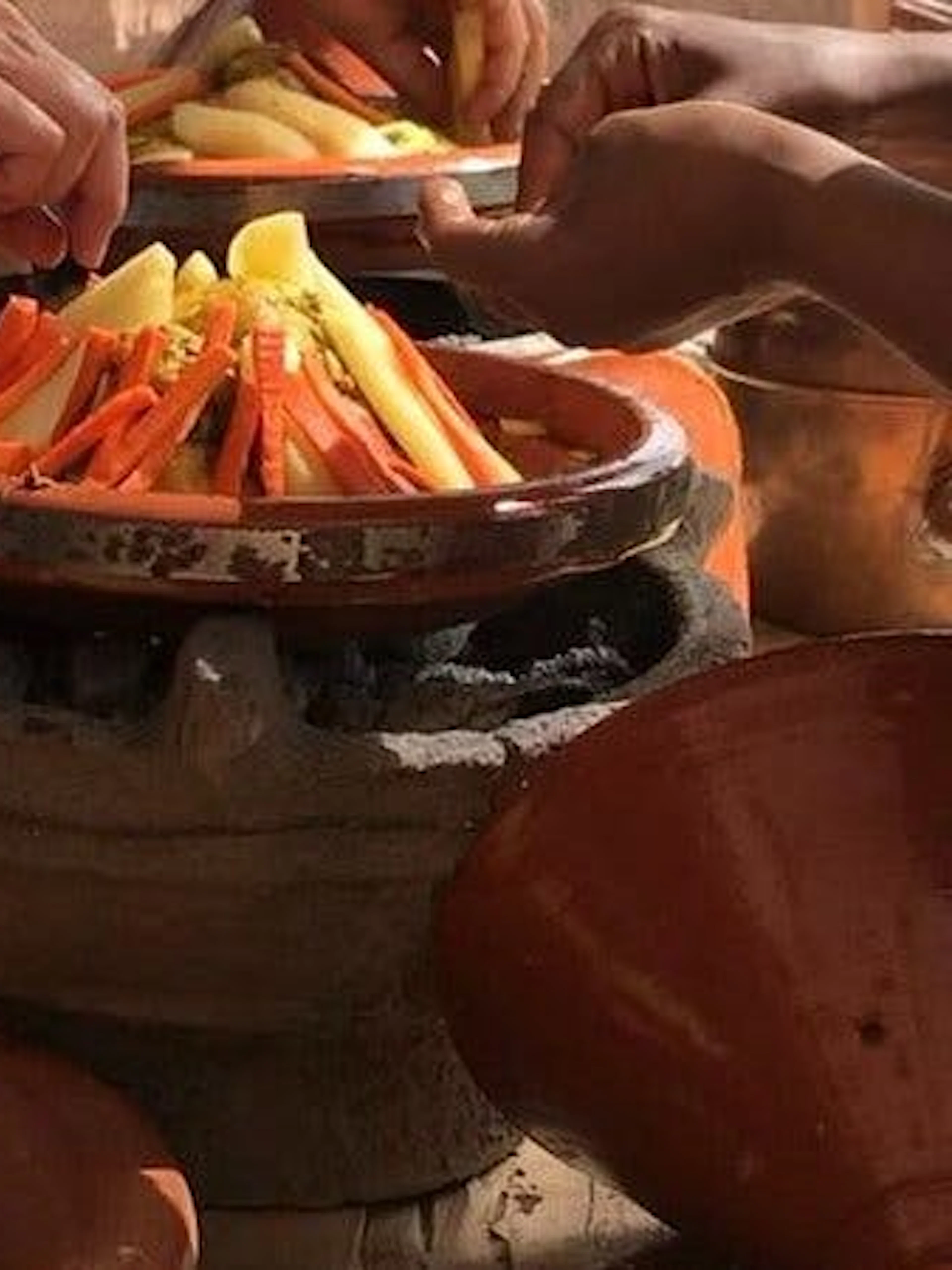 Hands preparing vegetables in a tagine during a Moroccan cooking class in Marrakesh.