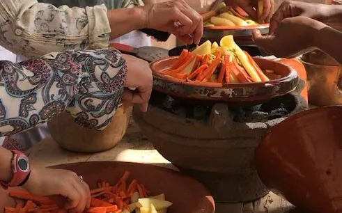 Hands preparing vegetables in a tagine during a Moroccan cooking class in Marrakesh.