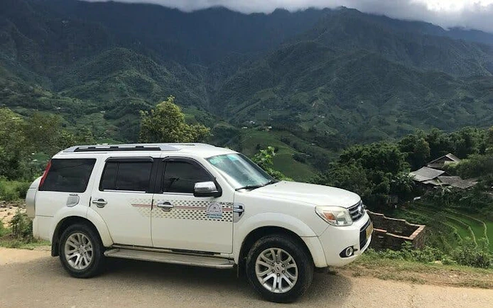 Private car on scenic route from Sapa to Ha Giang City with terraced rice fields.