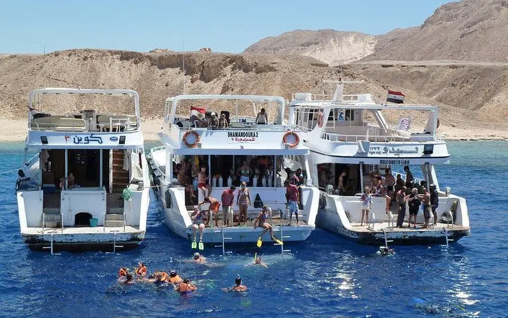 Snorkelers near boats at Tiran Island, Sharm El Sheikh, with desert backdrop.