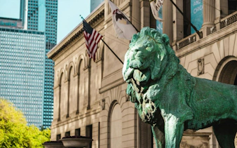 Lion statue at the entrance of the Art Institute of Chicago with flags in the background.