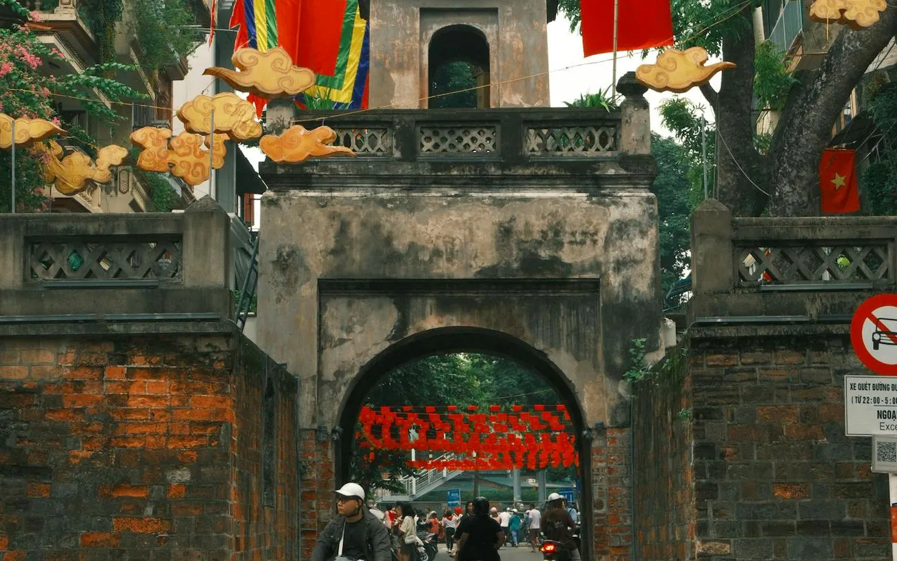 Ancient gate in Hanoi Old Quarter with motorbikes and pedestrians passing through.