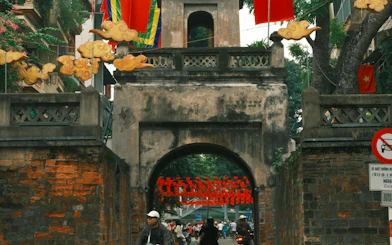 Ancient gate in Hanoi Old Quarter with motorbikes and pedestrians passing through.