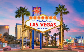 Las Vegas welcome sign with palm trees and cityscape in the background.