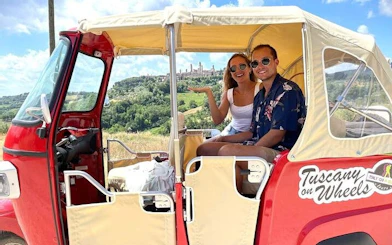 Tuk Tuk with tourists overlooking Tuscan countryside and San Gimignano skyline.