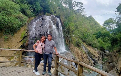 Couple at waterfall viewpoint in Cat Cat Village, Sa Pa, surrounded by lush greenery.