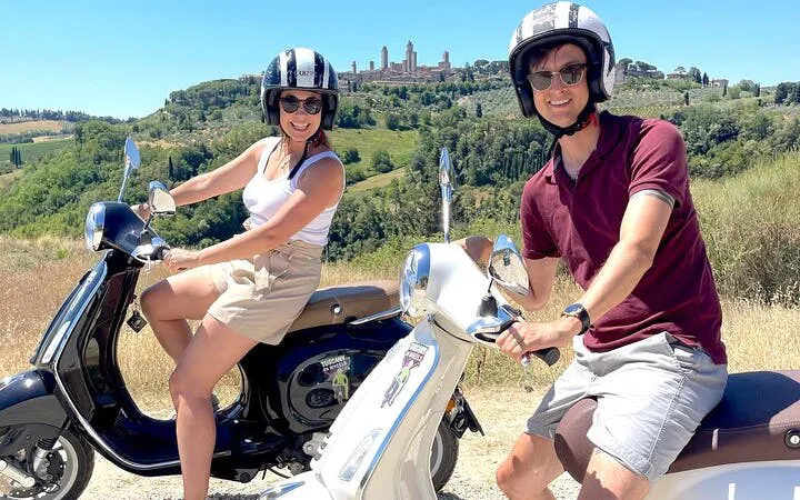 Couple riding Vespas through Chianti countryside with San Gimignano in the background.