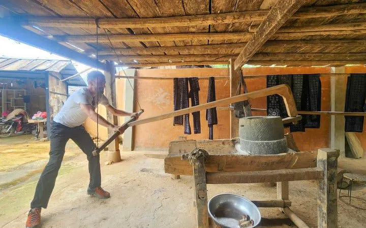Man operating traditional mill in Mu Cang Chai workshop with Hmong textiles in background.