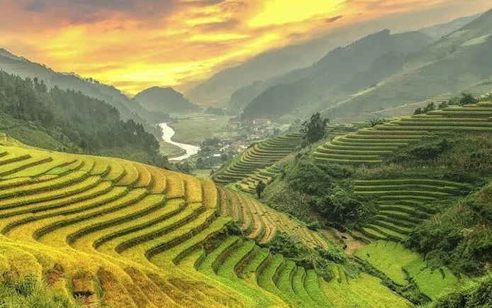 Terraced rice fields in Mu Cang Chai at sunset, with distant village and mountains.
