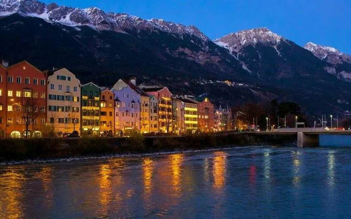 Colorful buildings along the Inn River with mountains in Innsbruck at dusk.