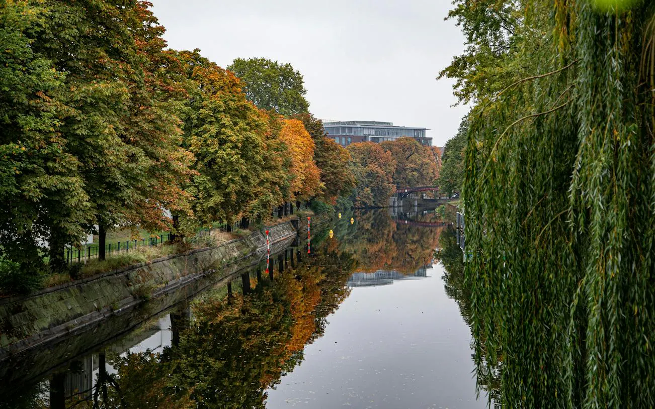Canal lined with autumn trees in Kreuzberg, Berlin, reflecting in the water.