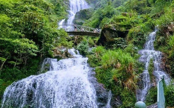 Waterfall with bridge in lush greenery, part of Sapa motorbike tour to Pusamcap Cave.