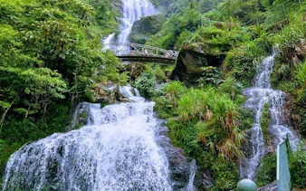 Waterfall with bridge in lush greenery, part of Sapa motorbike tour to Pusamcap Cave.