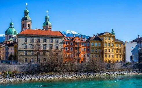 Colorful historic buildings along the Inn River with Alps in the background, Innsbruck.