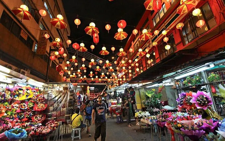 Lantern-lit street market in Kuala Lumpur with colorful stalls and visitors.