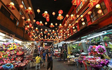 Lantern-lit street market in Kuala Lumpur with colorful stalls and visitors.