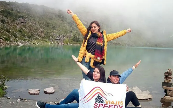 Trekkers posing by Humantay Lagoon with a tour banner, Cusco.