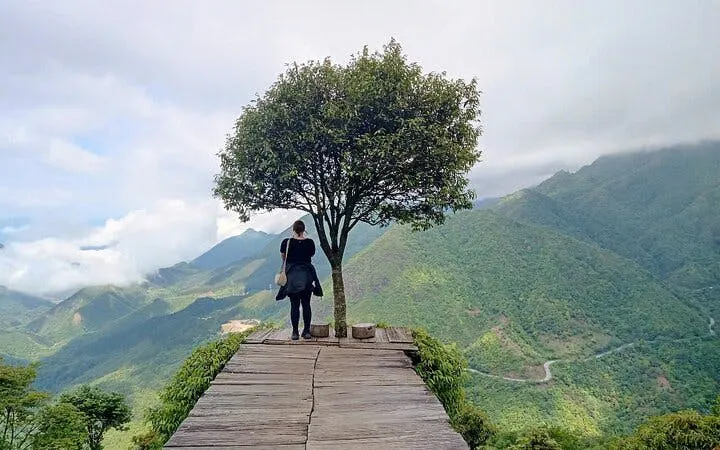 Person standing on a wooden platform overlooking lush mountains in Sapa, Vietnam.