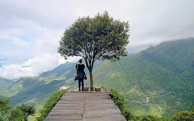 Person standing on a wooden platform overlooking lush mountains in Sapa, Vietnam.