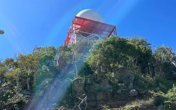 St. Maarten hike view with radar tower atop lush hill under clear sky.