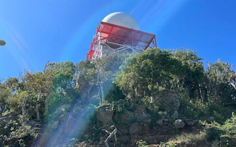 St. Maarten hike view with radar tower atop lush hill under clear sky.