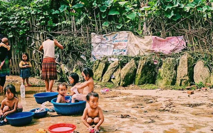 Children playing in water basins in Ta Van Village, Sapa, surrounded by lush greenery.