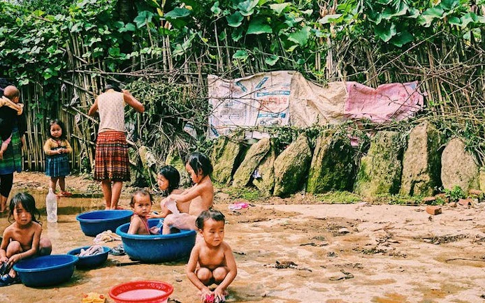 Children playing in water basins in Ta Van Village, Sapa, surrounded by lush greenery.