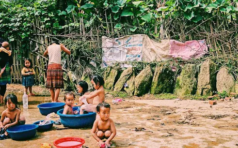Children playing in water basins in Ta Van Village, Sapa, surrounded by lush greenery.