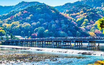 Togetsukyo Bridge over Katsura River with Arashiyama mountains in Kyoto during autumn.