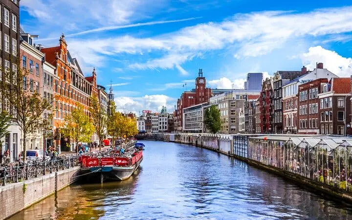 Amsterdam canal with boats and historic buildings, part of self-guided city exploration game.