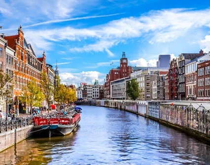 Amsterdam canal with boats and historic buildings, part of self-guided city exploration game.