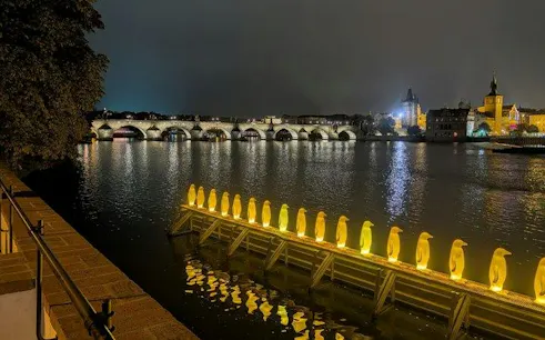 Prague night view with illuminated penguin sculptures on Vltava River, Charles Bridge in background.