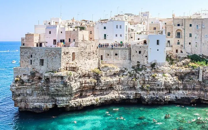 Polignano a Mare cliffside view with swimmers in turquoise sea, Valle d'Itria tour.