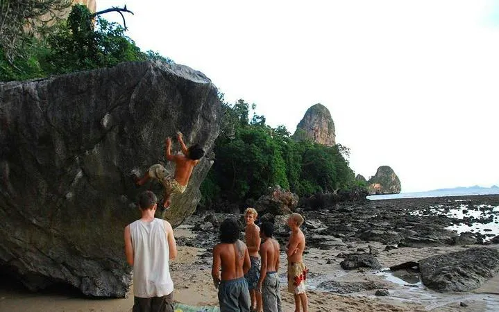 Rock climbers on boulder at Railay Beach, Krabi, with limestone cliffs in background.