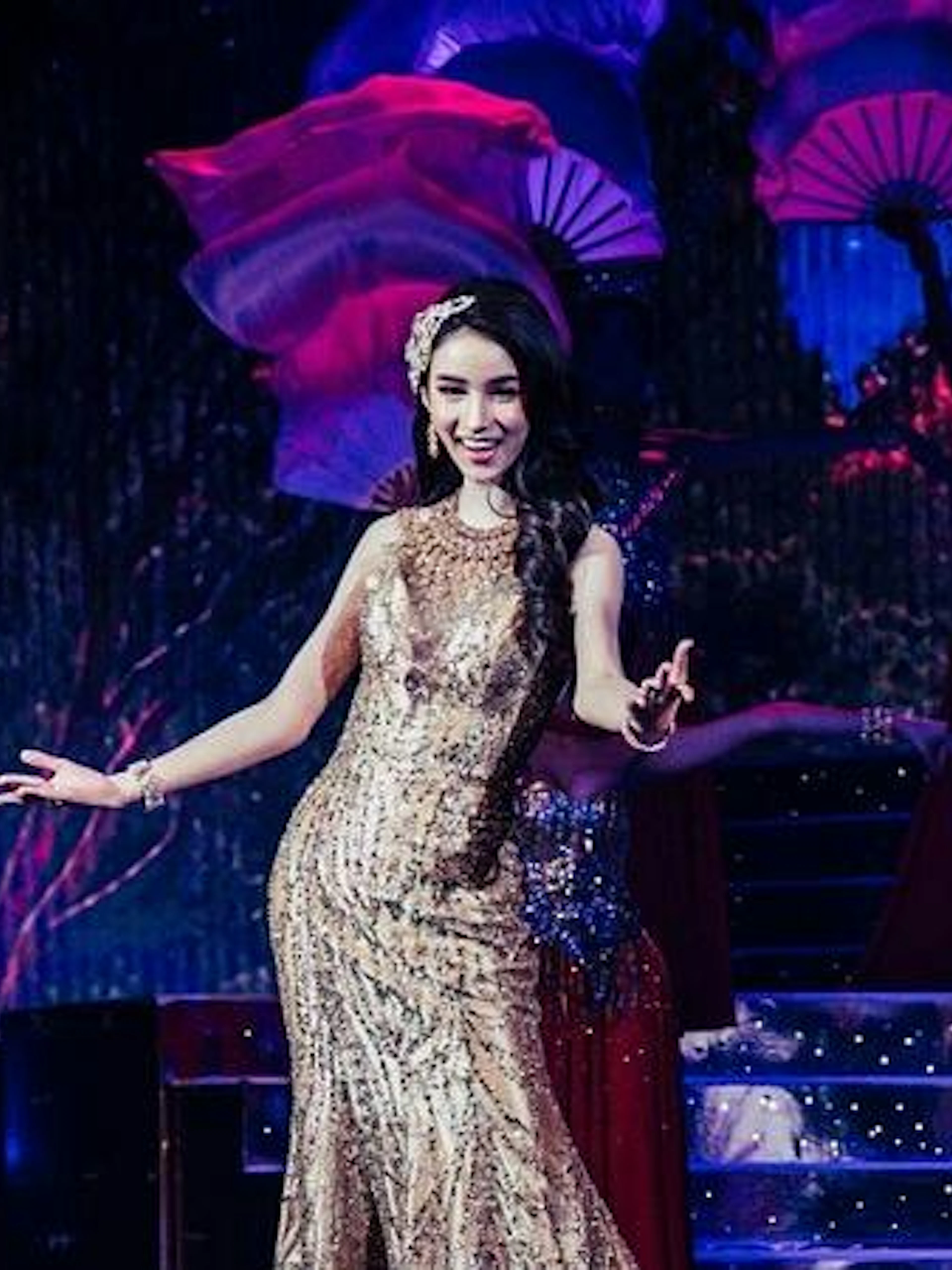 Performer on stage at Tiffany's Cabaret Show, Pattaya, with vibrant fans in the background.