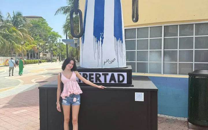 Woman standing by Cuban flag mural in Little Havana, Miami, during cultural walking tour.