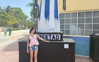 Woman standing by Cuban flag mural in Little Havana, Miami, during cultural walking tour.