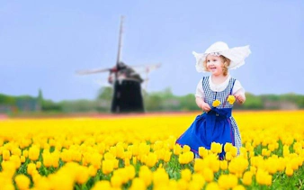 Child in traditional dress among tulips with windmill in Keukenhof Gardens, Netherlands.