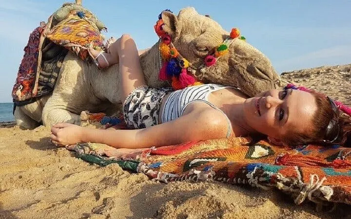 Camel resting on beach with colorful decorations, Sharm El Sheikh camel ride experience.