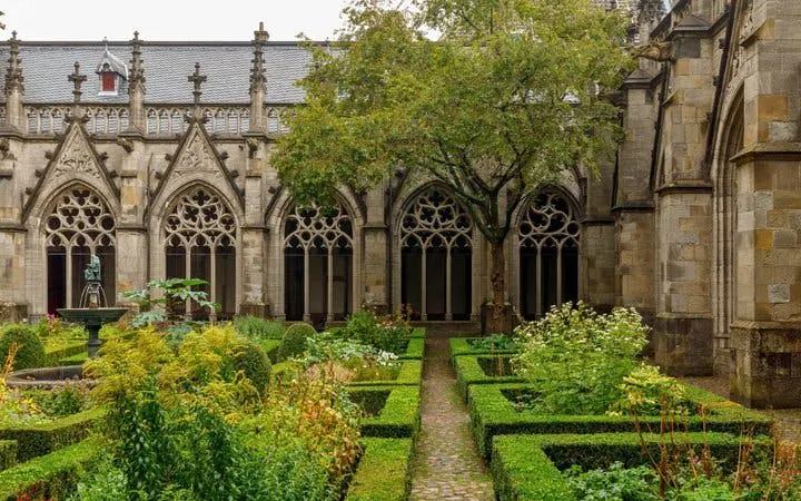 Cloister garden at Dom Church, Utrecht, with gothic arches and manicured hedges.