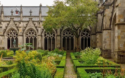 Cloister garden at Dom Church, Utrecht, with gothic arches and manicured hedges.