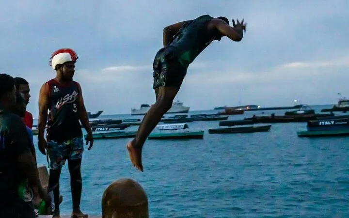 Diver jumping into the ocean at Stone Town Zanzibar Night Food Market with boats in the background.