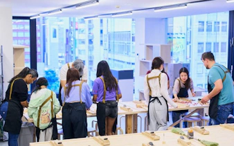 Participants crafting chopsticks in a Tokyo Shinjuku workshop, selecting wood and engraving kanji.